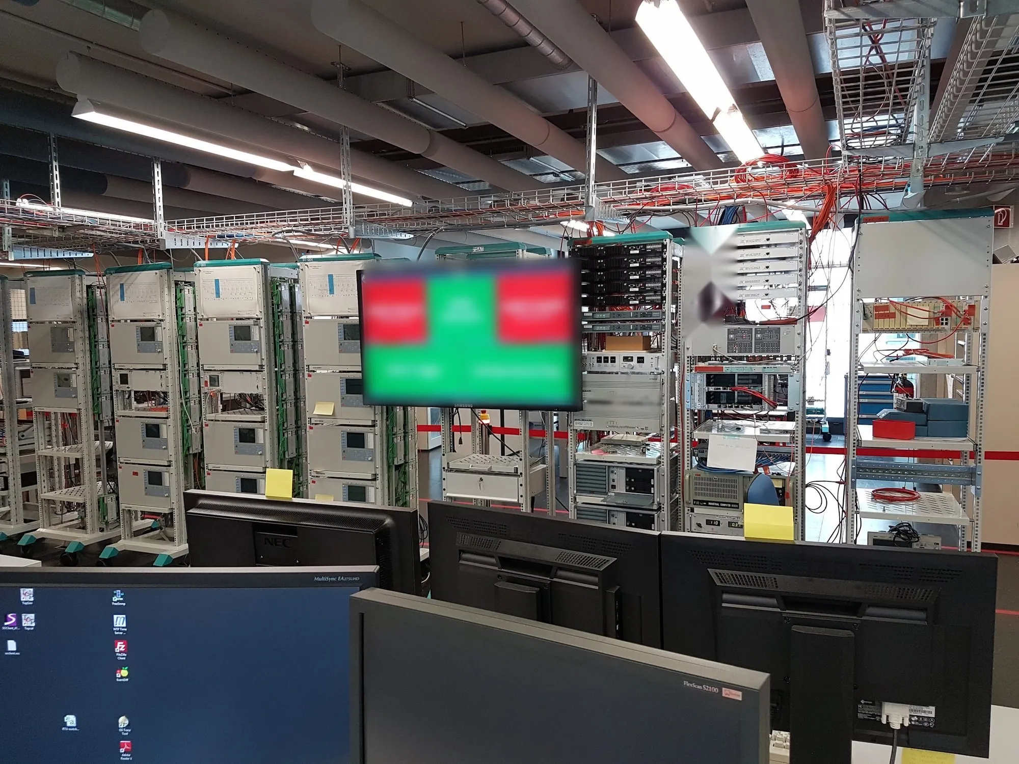 Prüflabor mit Racks voller Schutz- und Steuergeräte und einem Bildschirm mit Build-Status der automatisierten Tests